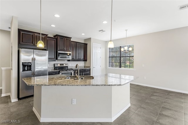 kitchen with light stone counters, an island with sink, dark brown cabinets, appliances with stainless steel finishes, and decorative light fixtures