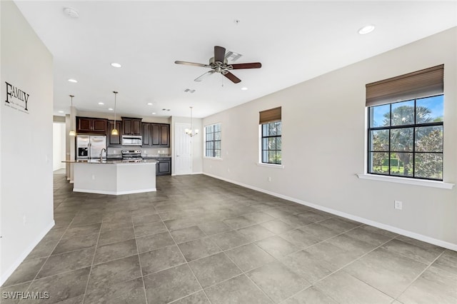 unfurnished living room with ceiling fan with notable chandelier, plenty of natural light, sink, and tile patterned flooring