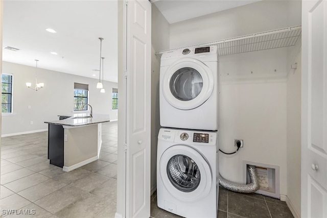 laundry room featuring stacked washing maching and dryer, a chandelier, sink, and light tile patterned floors