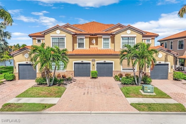 mediterranean / spanish home featuring driveway, stone siding, a tile roof, and stucco siding