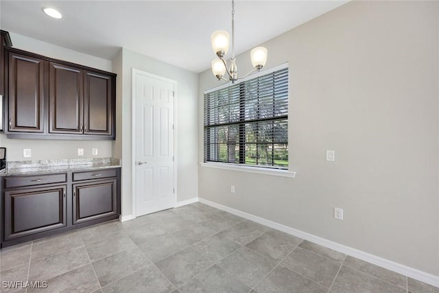 kitchen featuring light stone counters, baseboards, dark brown cabinets, decorative light fixtures, and an inviting chandelier