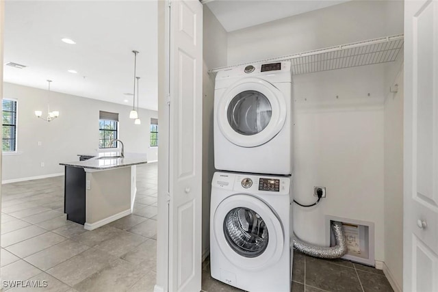 laundry area featuring laundry area, a sink, visible vents, stacked washing maching and dryer, and an inviting chandelier