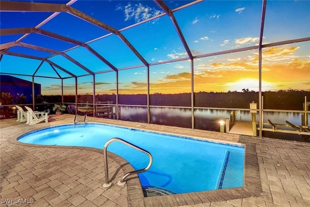 pool at dusk with glass enclosure, a water view, and a patio