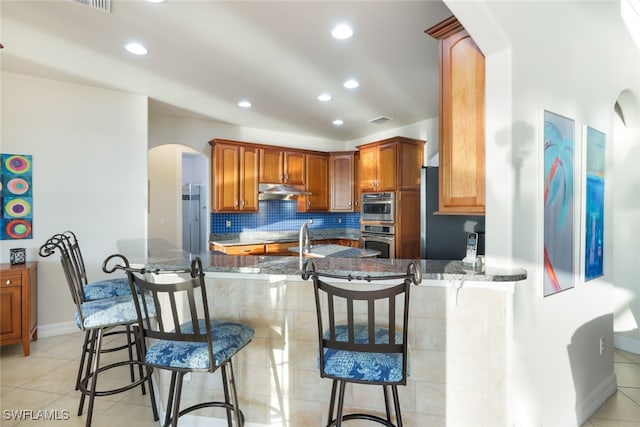 kitchen featuring a breakfast bar area, dark stone countertops, kitchen peninsula, and double oven