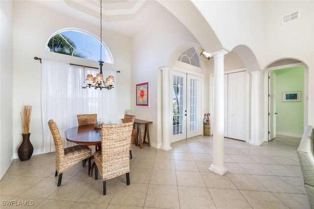 tiled dining space with a high ceiling, decorative columns, an inviting chandelier, and french doors