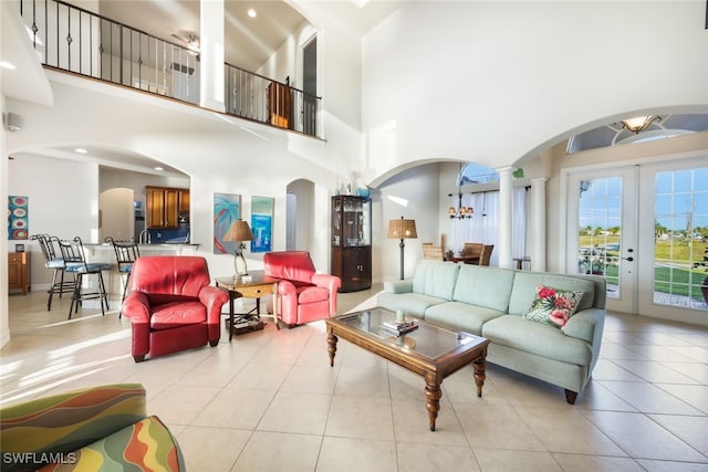 tiled living room featuring a towering ceiling, french doors, decorative columns, and an inviting chandelier