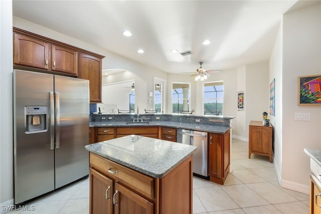 kitchen with dark stone counters, a center island, sink, ceiling fan, and appliances with stainless steel finishes