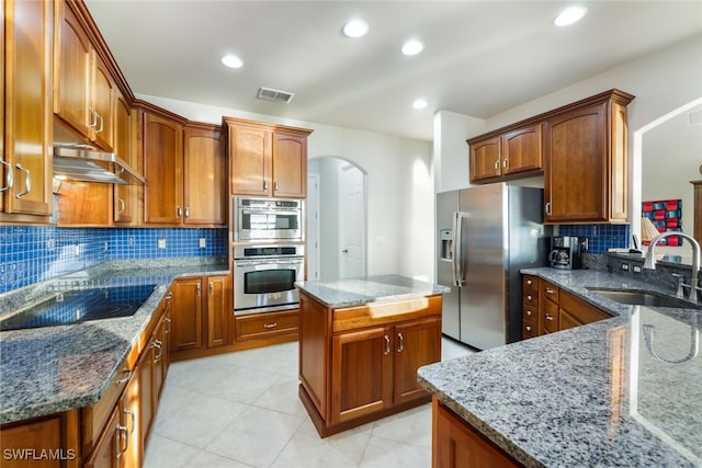 kitchen featuring stainless steel appliances, sink, a kitchen island, backsplash, and light stone countertops