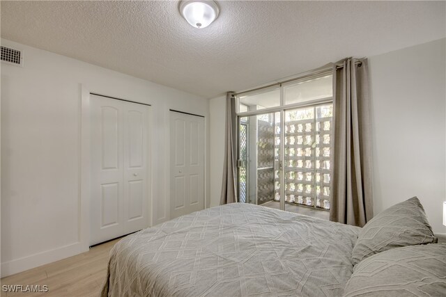 bedroom featuring a textured ceiling, light hardwood / wood-style flooring, and multiple windows