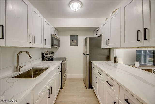 kitchen featuring sink, light wood-type flooring, appliances with stainless steel finishes, light stone counters, and white cabinetry