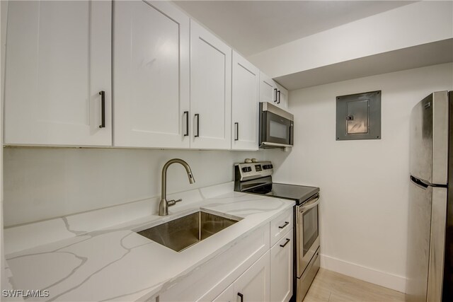 kitchen with white cabinetry, sink, light stone counters, light hardwood / wood-style floors, and appliances with stainless steel finishes