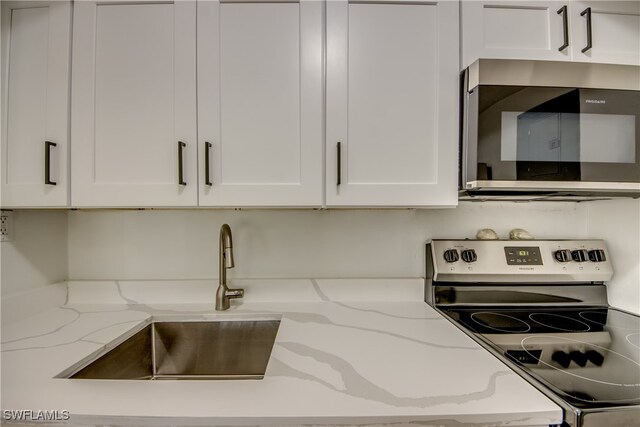 kitchen featuring white cabinets, appliances with stainless steel finishes, light stone countertops, and sink