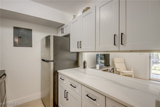 kitchen featuring electric panel, light stone countertops, light wood-type flooring, white cabinetry, and stainless steel refrigerator