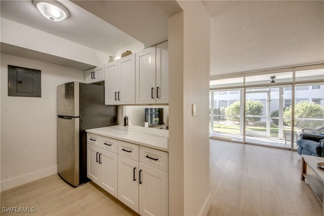 kitchen with light stone counters, light hardwood / wood-style flooring, electric panel, stainless steel fridge, and white cabinets