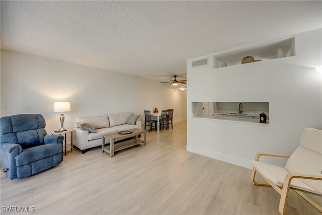 living room featuring ceiling fan, light hardwood / wood-style flooring, a textured ceiling, and sink