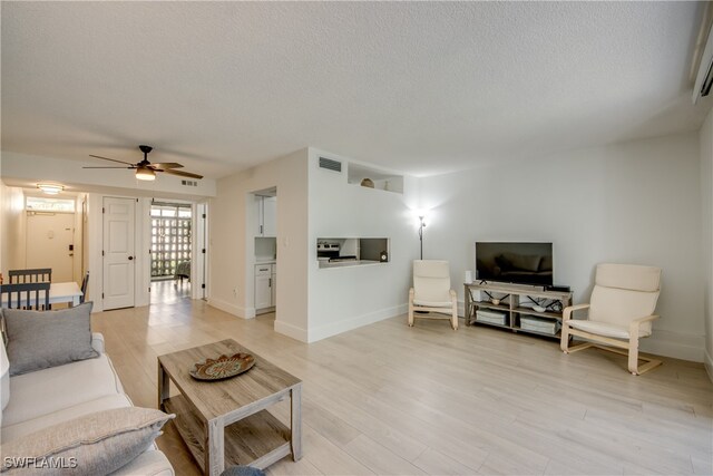 living room with ceiling fan, light hardwood / wood-style flooring, and a textured ceiling