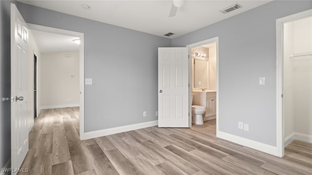 unfurnished bedroom featuring ensuite bath, ceiling fan, a closet, light hardwood / wood-style flooring, and a walk in closet