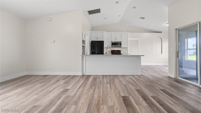 kitchen with white cabinetry, black fridge, light stone counters, lofted ceiling, and light wood-type flooring