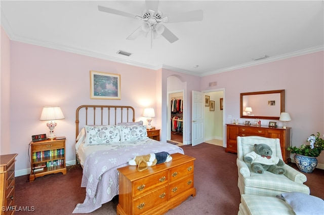 bedroom featuring a closet, a spacious closet, crown molding, dark colored carpet, and ceiling fan