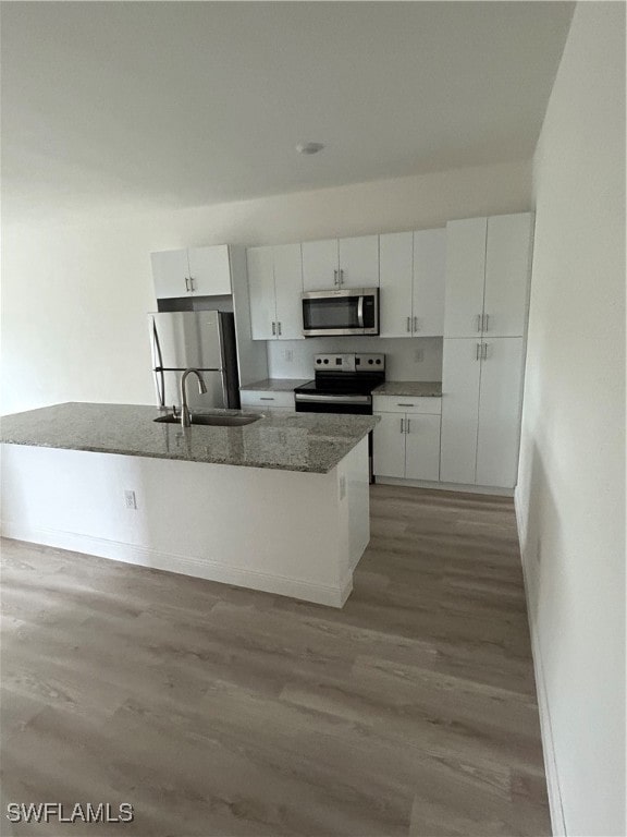 kitchen featuring light hardwood / wood-style floors, white cabinetry, appliances with stainless steel finishes, stone counters, and a kitchen island with sink