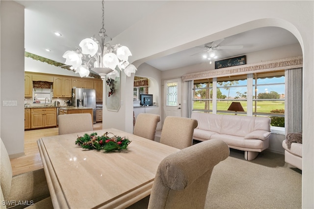 dining room featuring ceiling fan with notable chandelier, light hardwood / wood-style floors, sink, and vaulted ceiling