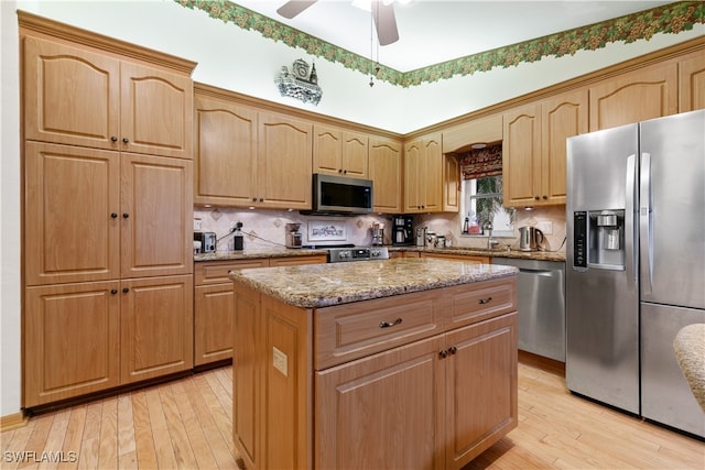 kitchen featuring a center island, light hardwood / wood-style flooring, ceiling fan, light stone countertops, and appliances with stainless steel finishes