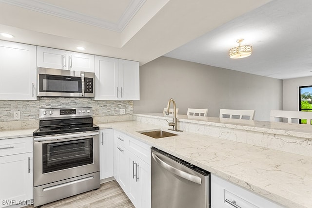 kitchen with ornamental molding, white cabinetry, appliances with stainless steel finishes, sink, and a breakfast bar area