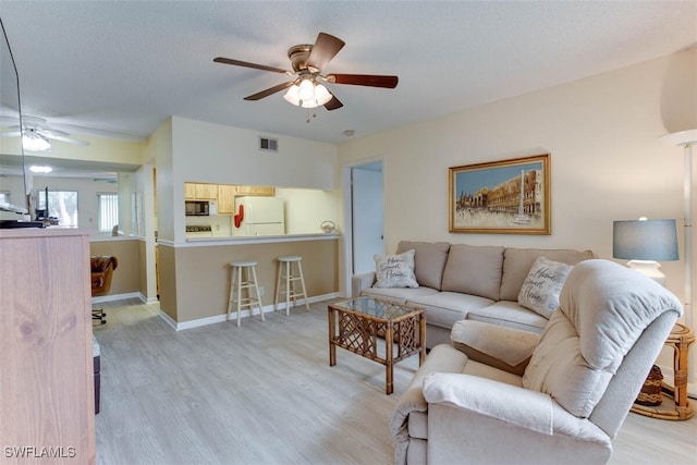 living room with a textured ceiling, ceiling fan, and light hardwood / wood-style flooring