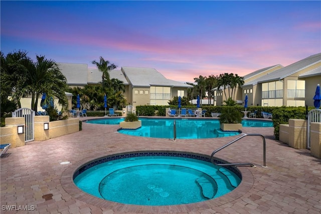 pool at dusk with a patio and a hot tub