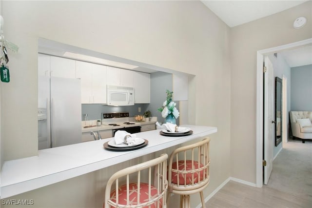 kitchen featuring white cabinets, a kitchen breakfast bar, white appliances, and kitchen peninsula