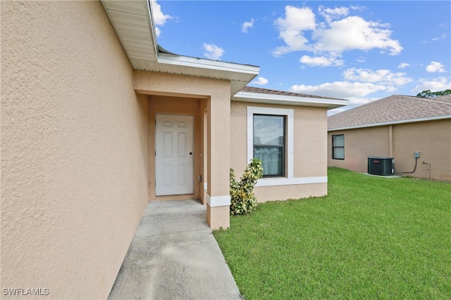 entrance to property featuring central AC unit and a lawn