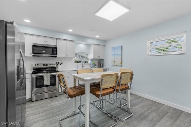 kitchen featuring light hardwood / wood-style floors, white cabinets, sink, backsplash, and appliances with stainless steel finishes