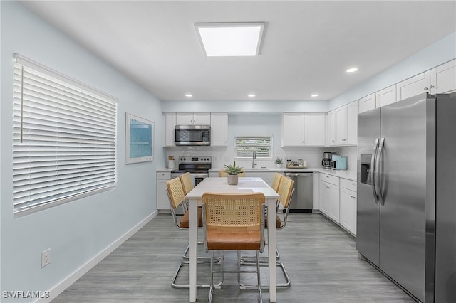 kitchen with sink, appliances with stainless steel finishes, backsplash, light hardwood / wood-style flooring, and white cabinets