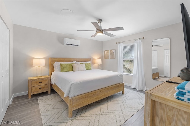 bedroom featuring a wall mounted AC, light hardwood / wood-style flooring, ceiling fan, and a closet