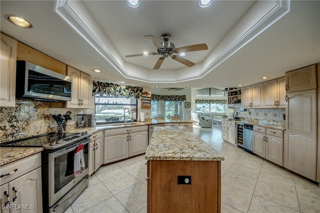 kitchen with stainless steel appliances, tasteful backsplash, a raised ceiling, a kitchen island, and light stone countertops