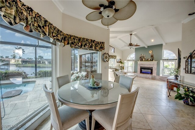 dining area featuring a fireplace, ceiling fan, light tile patterned floors, and a water view