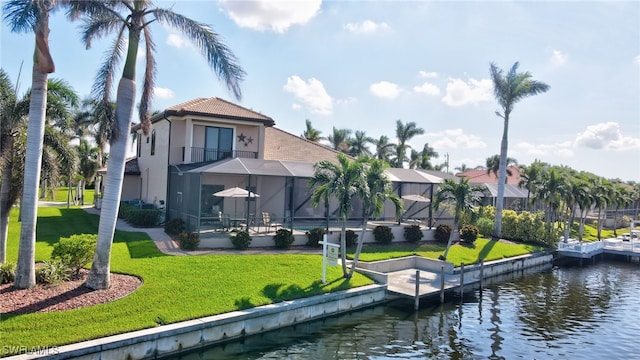 back of house featuring glass enclosure, a yard, and a water view