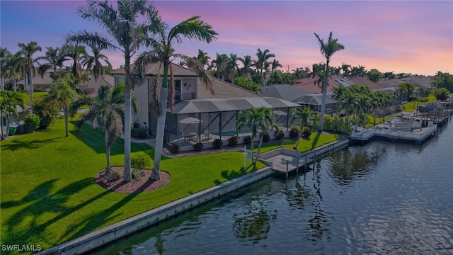 view of dock with a lanai, a lawn, and a water view