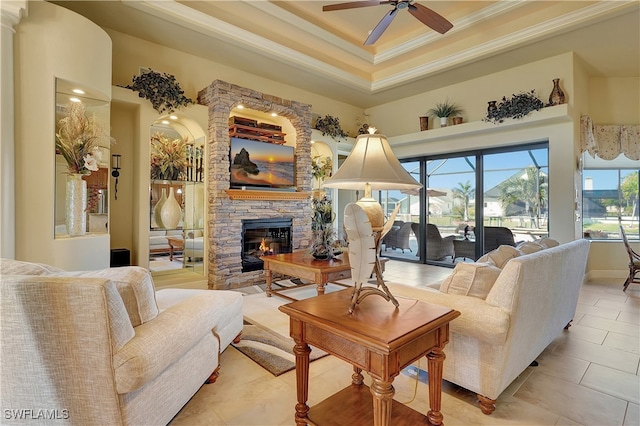 living room with ceiling fan, a raised ceiling, a fireplace, light tile patterned flooring, and ornamental molding