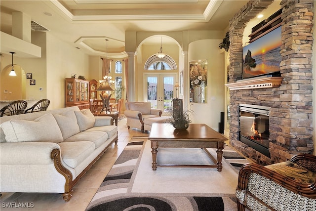 living room with french doors, decorative columns, a raised ceiling, a fireplace, and a chandelier