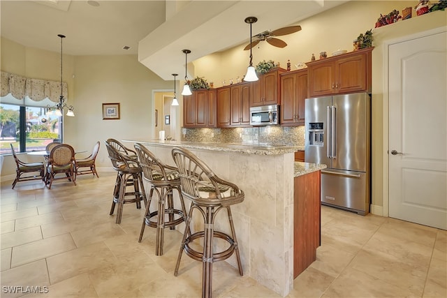 kitchen with light stone countertops, appliances with stainless steel finishes, a kitchen bar, ceiling fan, and decorative light fixtures