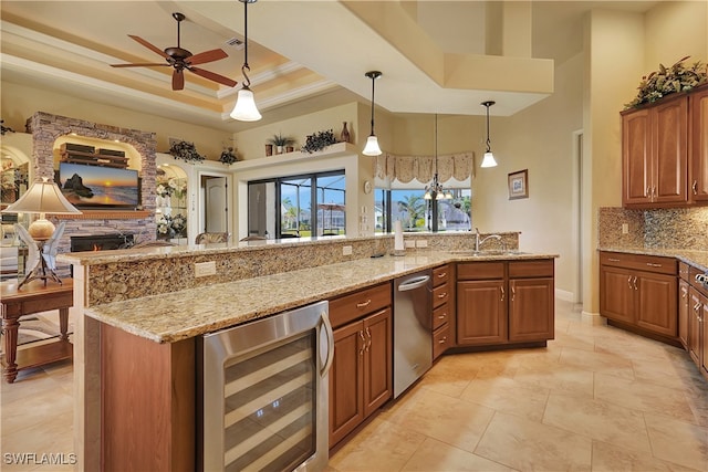 kitchen with a raised ceiling, hanging light fixtures, wine cooler, ornamental molding, and light stone counters