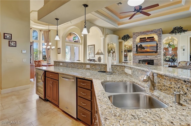 kitchen with light stone countertops, dishwasher, sink, a raised ceiling, and pendant lighting