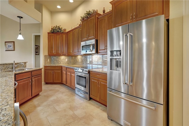 kitchen with sink, tasteful backsplash, light stone counters, pendant lighting, and appliances with stainless steel finishes