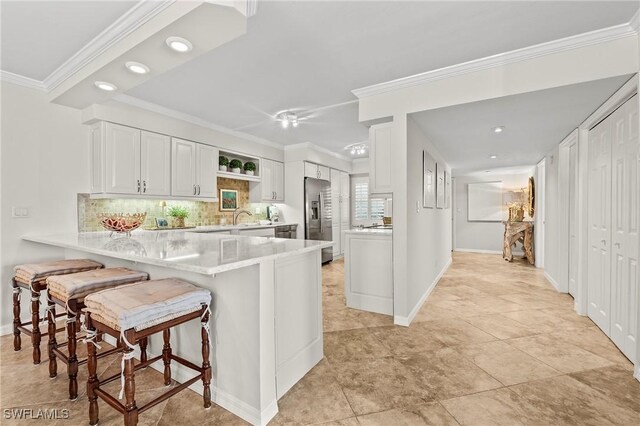 kitchen featuring white cabinetry, a breakfast bar, stainless steel fridge, and kitchen peninsula