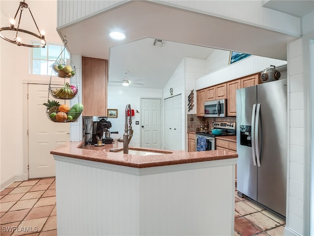 kitchen featuring ceiling fan with notable chandelier, kitchen peninsula, sink, tasteful backsplash, and appliances with stainless steel finishes