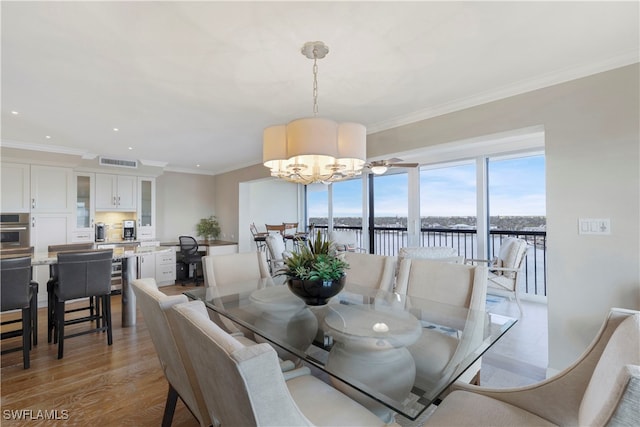 dining room with ornamental molding, light hardwood / wood-style flooring, a water view, and a notable chandelier