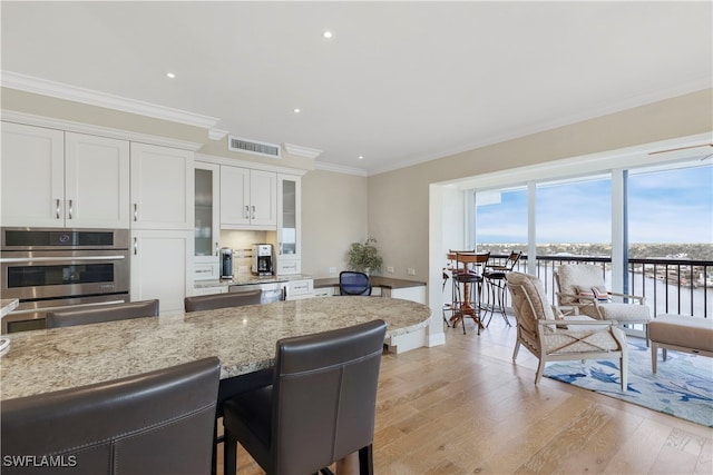 kitchen with ornamental molding, a kitchen breakfast bar, light stone countertops, light hardwood / wood-style flooring, and white cabinets