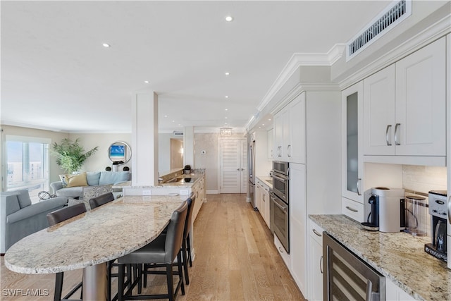 kitchen with light stone counters, wine cooler, a breakfast bar, white cabinets, and light hardwood / wood-style flooring