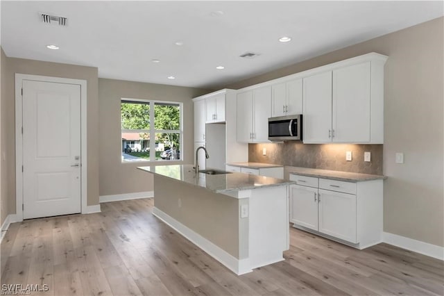 kitchen featuring light hardwood / wood-style flooring, white cabinets, sink, and a kitchen island with sink